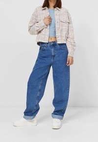 Geknipte, gemusterde jas in lichte tinten met knoopsluiting; gecombineerd met losse, blauwe denim jeans en witte sneakers.