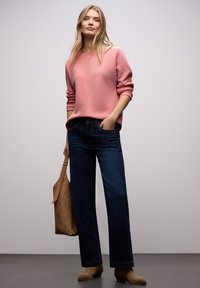 Suéter de manga larga con rayas rosas y un patrón texturizado, combinado con vaqueros de pierna ancha azul oscuro y botines beige, sosteniendo un bolso marrón.