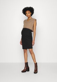 Colete castanho tricotado com bordas em forma de ondas, combinado com uma saia preta canelada. Modelo usa botas de tornozelo castanhas brilhantes com tacões quadrados.