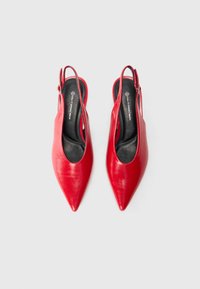 Escarpins rouge en cuir avec un bout pointu, une texture lisse et une semelle intérieure noire. Dispose d'une fine bride ajustable au talon.