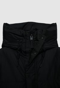 Giubbotto imbottito nero con cappuccio, colletto alto, chiusura con zip, cordoncini e cuciture decorative. Presenta una texture liscia e opaca.