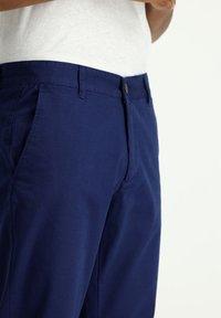 Pantalones de algodón azul marino con diseño de frente plano, bolsillos laterales y cierre de botón único. Textura suave con un detalle mínimo.