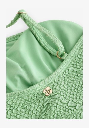 Zelená textília s textúrovaným tkaním, hladká vnútorná podšívka, čipkované ramienka a zlatý strapec ako akcent na výstrihu.