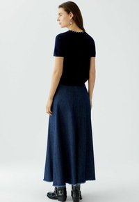 Marineblaues Oberteil mit kurzen Ärmeln und dekorativen Knöpfen am Rücken, kombiniert mit einem langen Denim-Rock mit fransigem Saum und schwarzen Stiefeletten.