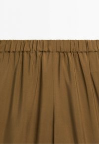 Brown elastic waistband pants with gathered fabric detail and visible stitching along the waistline.
