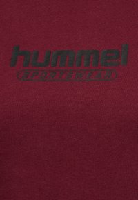 Bordeaux t-shirt med et sort "hummel" logo og ordet "SPORTSWEAR" i fed, simpel typografi på fronten. Fremstillet med en glat tekstur.