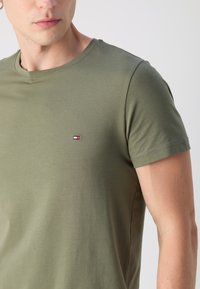Olivegrünes Baumwoll-T-Shirt mit Rundhalsausschnitt, kurzen Ärmeln und kleinem, gesticktem Logo auf der Brust. Weiche Textur, figurbetonter Schnitt.