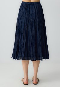 Gonna plissettata blu navy realizzata in tessuto leggero; vita elastica; lunghezza a metà polpaccio; superficie testurizzata con righe verticali e volume.