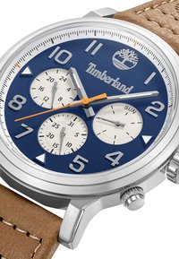 Orologio in acciaio inossidabile con quadrante blu, sottodial bianchi, dettagli arancioni e cinturino in pelle marrone. Presenta numeri in grassetto e indicatore del giorno.