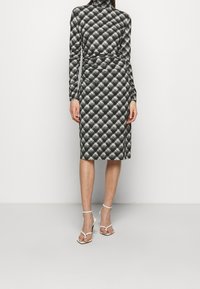 Czarna i biała sukienka w wzory z długimi rękawami, golfem, dopasowaną sylwetką i długością do kolan. Posiada fakturowany wzór w romby.