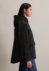 Zwarte hoodie-jak met een relaxte pasvorm, voorzien van een voorzak en drukknoopmanchetten, gemaakt van een gladde, duurzame stof.