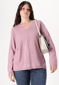 Ροζ πουλόβερ με V λαιμόκοψη, πλέξη με καλώδιο, ριμπ μανσέτες και στρίφωμα. Συνδυασμένο με μία ανοιχτό γκρίζα τσάντα ώμου και μπλε τζιν.