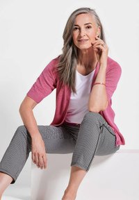 Rosa kurzärmelige Strickjacke über einem weißen Oberteil, kombiniert mit schwarz-weißen karierten Hosen, die eine schmale Passform und eine subtile Textur aufweisen.