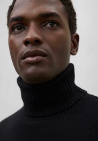 Schwarzer, gerippter Rollkragenpullover mit hohem Kragen. Nahaufnahme des Gesichts mit glatter Haut und neutralem Ausdruck. Einfacher, strukturierter Stoff.