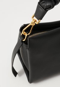 Schwarze Leder-Handtasche mit einem goldfarbenen Verschluss und Reißverschluss, einer strukturierten und texturierten Körperform sowie einem eleganten, minimalistischen Design.