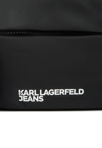 Geantă din material texturat negru, prevăzută cu închidere cu fermoar și branding alb îndrăzneț „KARL LAGERFELD JEANS” de-a lungul marginii inferioare.