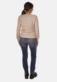 Suéter de punto beige con un patrón texturizado en la parte trasera, dobladillo acanalado, usado sobre jeans azules. Botas de plataforma negras visibles en la parte inferior.