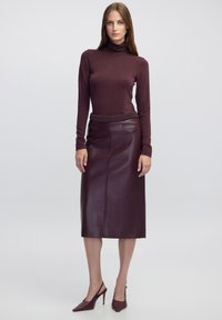 Bordeaux leren midirok met een getailleerde silhouette, zijnaaden en een klein zakje; gecombineerd met een bijpassende coltrui met lange mouwen.