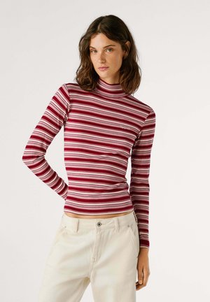Rood en roze gestreepte langemouwen turtleneck top met een aansluitend ontwerp en ribbeltextuur, gecombineerd met lichtgekleurde broeken.