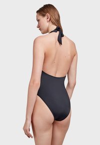 Bañador de una pieza negro con cuello halter, espalda baja y pierna alta. Textura suave y cierre de lazo en el cuello.