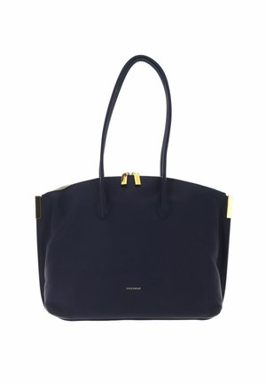 Sac cabas en cuir bleu foncé avec deux longues anses, tirettes de fermeture éclair dorées, et petit logo doré de la marque "Coccinelle" à l'avant.