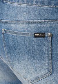 Jasnoniebieska kieszeń z denimu z widocznym przeszyciem, metalowym nitem i czarną metką z napisem "ONLY UNIQUE DENIM WEAR".