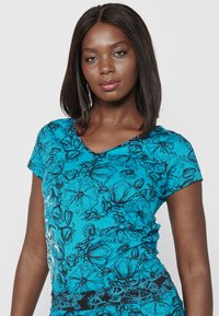 T-shirt turquoise à col en V avec un motif floral noir, manches courtes et une coupe confortable avec une texture de tissu douce.