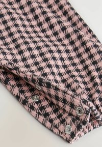 Primo piano di un tessuto a scacchi rosa e nero, caratterizzato da bottoni a scatto in argento e da un materiale a maglia morbido e texturizzato.