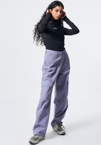 Schwarzes Langarmoberteil mit weißem Logo, kombiniert mit helllila Cargo-Hosen mit Seitentaschen und grauen Turnschuhen mit dunklen Akzenten.