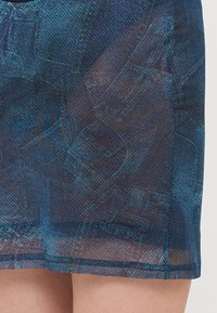Tejido azul con un patrón y un acabado texturizado, que presenta una superposición semitransparente en el dobladillo. El diseño incluye tonos de azul oscuro y claro.