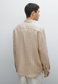 Light brown striped shirt in a relaxed fit, made from textured fabric. Features a pointed collar and buttoned cuffs. Back view shown.