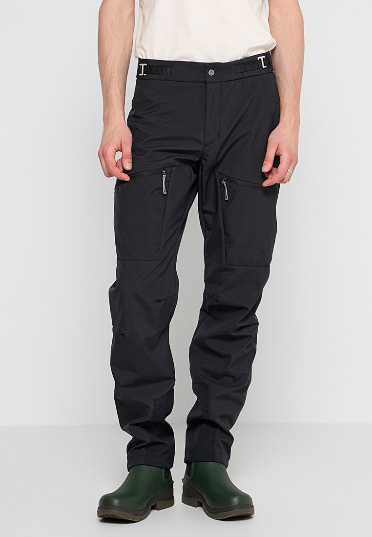 Schwarze wasserdichte Hose mit mehreren Reißverschlusstaschen, verstellbarem Bund und schmal zulaufenden Beinen. Das Material wirkt robust und leicht.