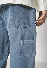 Light blue denim cargo pants featuring multiple pockets, a textured surface, and a relaxed fit. The fabric shows visible stitching details.