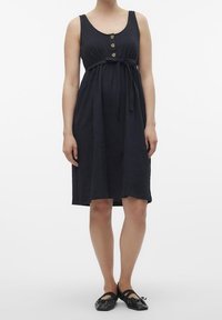 Marinblå ärmlös klänning med knälång nederdel, med en knappframsida, knytbälte och subtil tygtextur; matchad med svarta ballerinaskor.