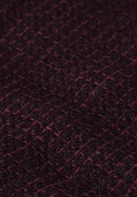 Gelaagd stof in diep bordeauxrood met een verhoogd, geweven patroon dat een rasterachtig ontwerp creëert, waardoor de tastbare kwaliteit wordt versterkt.