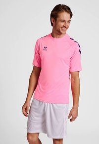 Rosa kortärmad sporttröja med marinblå detaljer på axlarna. Matchas med vita shorts, gjorda av lätt, andningsbart tyg.