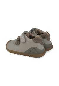 Zapatos de niño grises con parte superior lisa, acentos marrones en contraste, doble correa de velcro y suelas de goma texturizadas.
