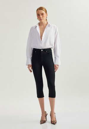 Mustat denim capri-housut korkealla vyötäröllä, joissa on edessä nappisuljenta ja takataskut. Yhdistetty valkoiseen nappikauluspaitaan.