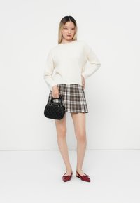Kremowy sweter, spódnica w kratę w brązowych i białych odcieniach, czarna torebka o fakturowej powierzchni i czerwone płaskie buty. Czysty, minimalistyczny design na białym tle.