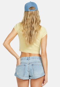T-shirt jaune court à manches courtes, associé à un short en jean bleu clair. Le short a des ourlets retournés et des poches arrière.