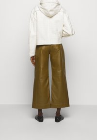 Przycięty, biały, teksturowany hoodie z kapturem, zestawiony z oliwkowymi, szerokimi spodniami skórzanymi. Czarne buty typu slip-on dopełniają całość.