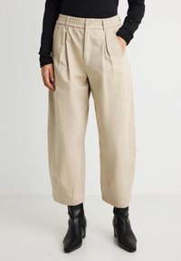 Μπεζ παντελόνι ψηλόμεσο cropped με πιέτες, πλαϊνές τσέπες και κούμπωμα με κουμπί, συνδυασμένο με μαύρο μακρυμάνικο τοπ και μαύρα μποτάκια με τακούνι.