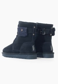 Botas de ante azul marino hasta el tobillo con forro de piel de oveja, que presentan un detalle de denim, botones de metal y una hebilla en la correa. Suela de goma texturizada.