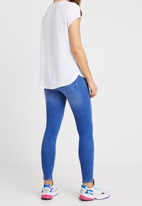 Weißes kurzärmeliges Bluse mit abgerundetem Saum, kombiniert mit blauen Skinny Jeans und weißen Sneakers mit Akzenten in Pink und Blau.
