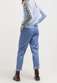 Pull rayé bleu clair avec des manches à imprimé léopard, détail de fermeture éclair au dos ; associé à un pantalon bleu clair et des bottines brunes.