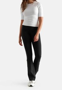Top corto bianco aderente a maniche corte e leggings neri a zampa, entrambi realizzati in tessuto liscio. Scarpe sportive bianche con dettagli grigio chiaro.