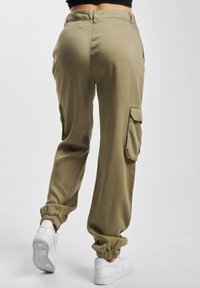 Oliven grøn cargo bukser med sidelommer, elastiske manchetter og en afslappet pasform, parret med hvide sneakers.
