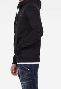 Svart hoodie med dragsko, framficka och ribbade mudd. Bärs med mörkblå jeans och visar en avslappnad, figursydd design.