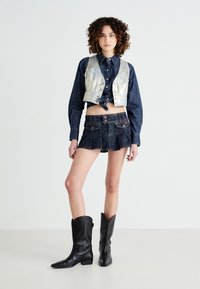 Denim crop top with silver accents, matching dark denim shorts with pleats, and black leather cowboy boots. Neutral background.