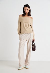 Beige off-shoulder sweater, cream pleated trousers, mint green sneakers, and a small brown handbag. Smooth textures and minimal design.